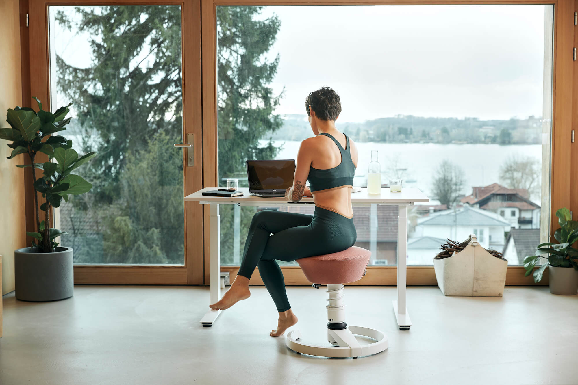 Woman sitting in her home office on the active office chair Aeris Swopper, with a view of a lake.