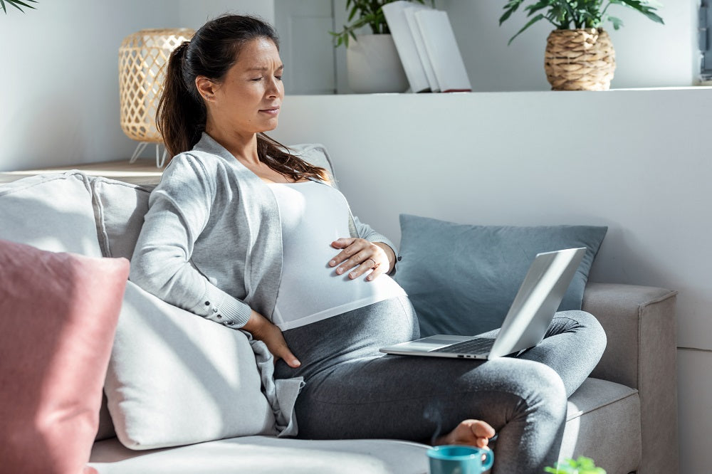 Une femme enceinte assise dans son bureau à domicile avec des douleurs au dos
