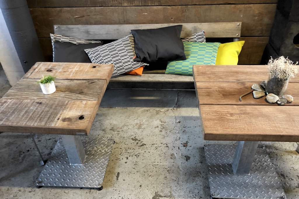 zwei kleine Tische aus Massivholz und eine Sitzbank mit bunten Kissen