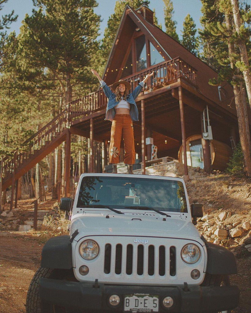 Court standing on her white jeep in front of a a-frame cabin