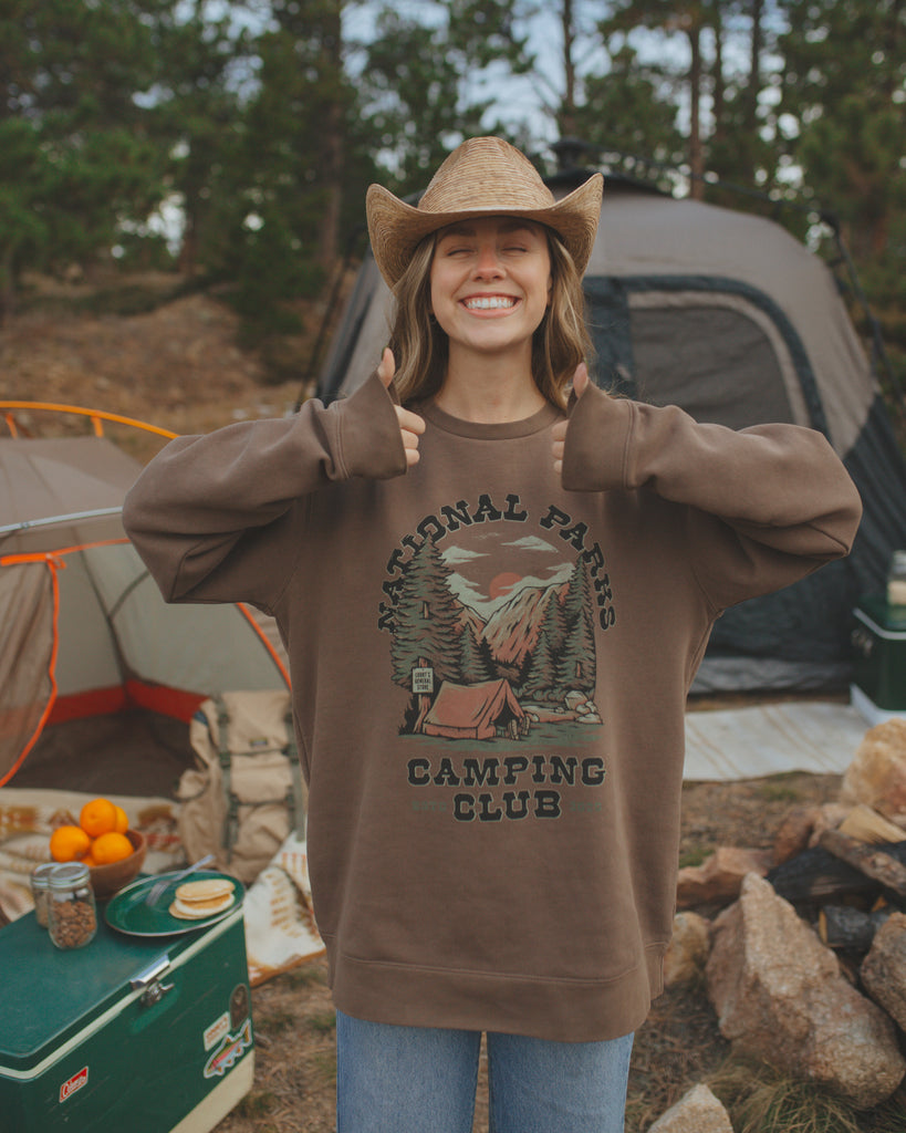 Court giving a thumbs up in front of a tent wearing the camp club crewneck