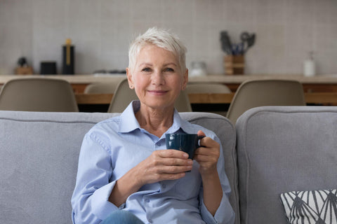 Happy calm carefree middle aged lady enjoying fresh tasty coffee at home