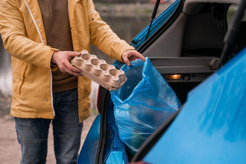 Man holding carton container near blue trash bag in car