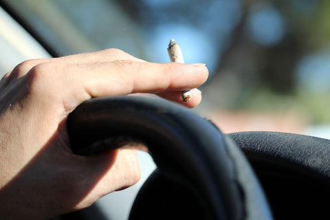 Person smoking joint in car, holding joint and steering wheel with left hand. 