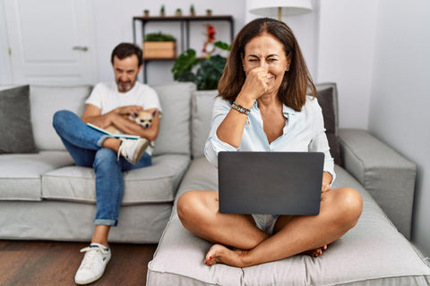 Woman using laptop smelling something stinky and disgusting, intolerable smell, holding breath with fingers on nose.