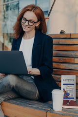 Professional sitting on a bench, using their laptop and a cup and bag of Barnie's Mocha Blueberry.