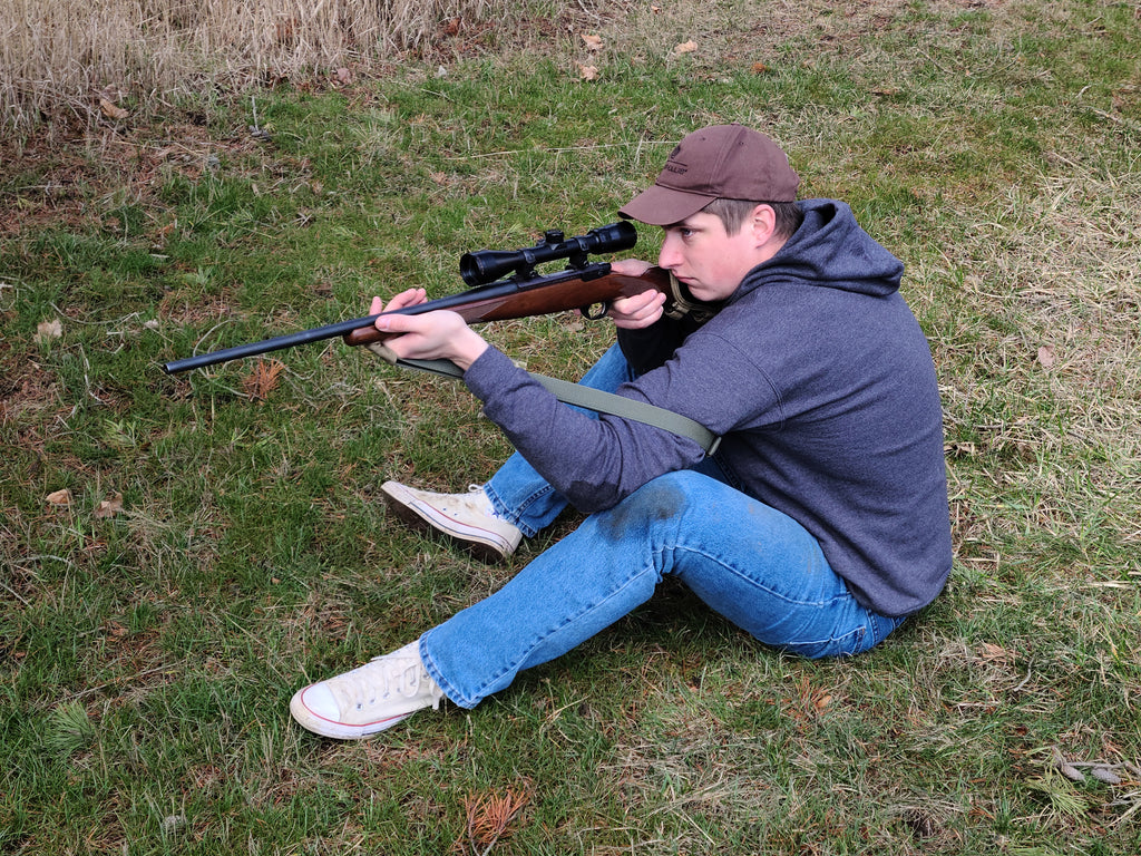 RifleCraft owner demonstrating a seated shooting position with his green nylon webbing shooting sling and hunting rifle