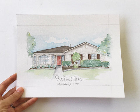 Hand holding a watercolor painting of a white house with red front door