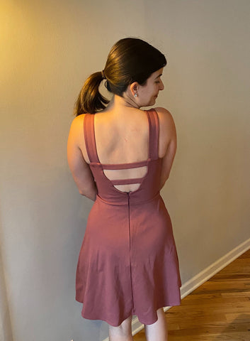 back view of Heather in front of a gray wall in pink a-line dress with open back and two cross back straps