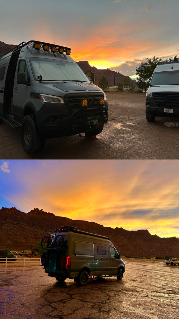 Three Revel adventure vans are in a parking lot in Utah; the sun is setting behind red hills in bursts of orange and red.  One van has an Owl Van’s B2 Rack with a Monster XL Cargo Box.