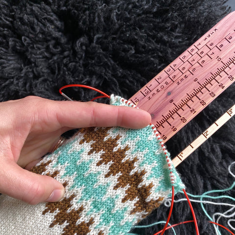 caucasian woman's hand holding an unfinished knit sock on the sock ruler to demonstrate use