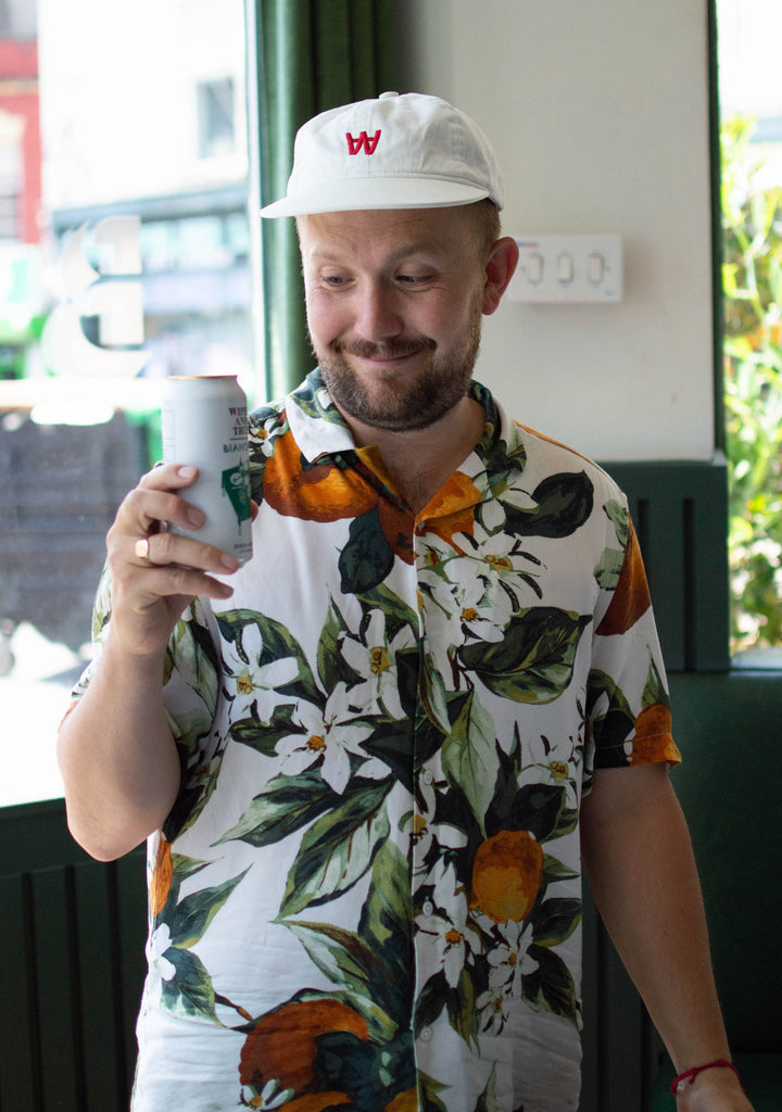 A man wearing a cap and a colourful shirt smiles at a can of beer