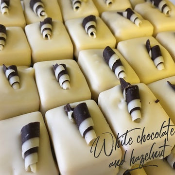 Photo of lots of rectangular white chocolate Belgian chocolates topped with chocolate curls