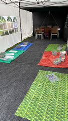 Photo of the PAPILIO Summer Fun tent set up for craft activities. Plastic mats are laid out with different craft activities and resources laid out on them. A set of tables and chairs can be see at the end of the tent.