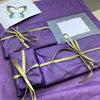 A wrapped letterbox gift in purple tissue and green raffia ready for posting.