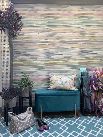 A photo of an entryway with statement wallpaper. The bench, rug, cushion and plants all co-ordinate with the wallpaper. The colours are teals, purples and greens.