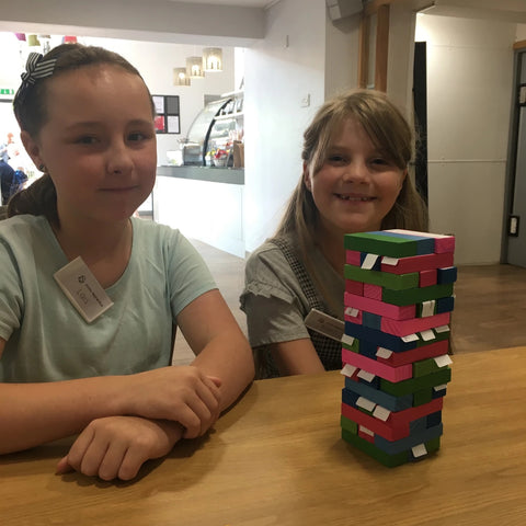 Photo of two girls with a multi-coloured jenga tower in front of them. The blocks have labels on them on which they've written important parts of customer service.