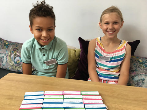 Photo of a ten year old boy and girl sitting behind multi-coloured jingo blocks. On the blocks are labels on which are written important aspects of customer service.