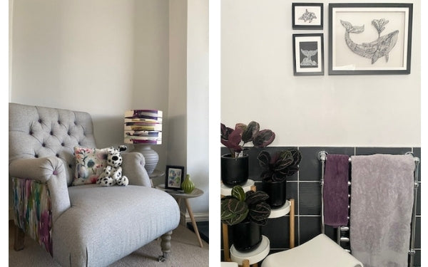 Two images. The first photo is of an armchair next to two side tables. One side table has a lamp with a shade with abstract horizontal strokes in purples, blues and green. The chair has one fabric on the seat and a patterned, multicolour fabric on the sides. A photo of a bathroom. Three black and white, handmade pictures of a whale and dolphins are on the light grey upper wall. A towel rail below them has a large grey towel and a smaller aubergine one. On the left of the photo is a tiered plant stand with 3 purple and black calathea plants. Just in shot between the plants and towel rail is a white stool. The lower part of the wall is dark grey tiles.