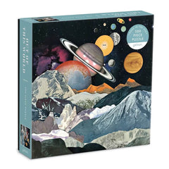 Photo of the box of the Galison 500 piece puzzle; Out of this world. The puzzle image is a from a paper cut piece of artwork o the moon surface with other planets visible in a line in the sky.