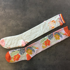 Photo of two knee high socks from Powder. One is pale blue with a unicorn image at the top. The other is light lilac with tropical leaves all over it.