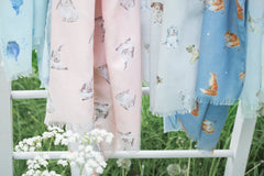 Photo of the ends of 5 lightweight scarves by Wrendale designs. They are hanging on a ladder in a field.