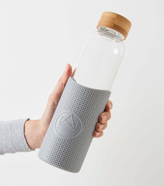A hand is holding the Forever Young grey reusable water bottle, with a silicone grip and bamboo lid.