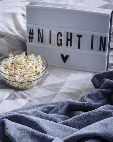 a picture of a small lightboard with the words night in on top of a duvet next to a bowl of popcorn