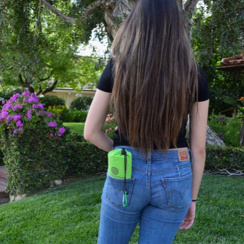 a college student on a college campus with a green ECCOSOPHY pocket blanket. The folded beach blanket is in its travel pouch and is small enough to fit in the students pocket. It comes with a matching carabiner so you can hang it on your backpack.