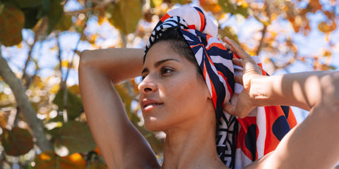 A beautiful young woman drying her hair with an ECCOSOPHY quick dry orange microfiber beach towel.