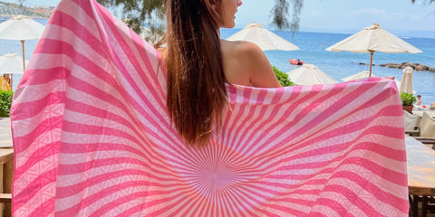 A young lady holding a stripped pink microfiber beach towel from ECCOSOPHY. The quick dry towel is baby pink and hot pink stripped.