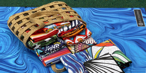 a beach bag next to a swimming pool full of ECCOSOPHY microfiber beach towels in vibrant colors. 