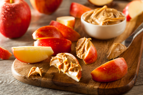 slices of apple with peanut butter on them sit on a wooden cutting board