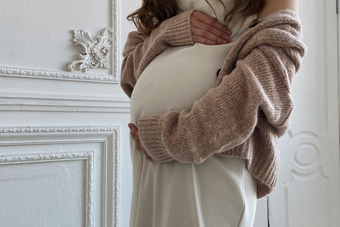 a pregnant person holds their belly wearing a sweater and a white dress
