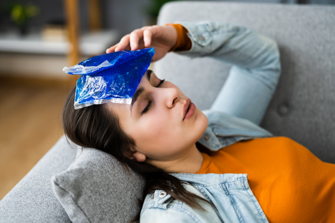 a person lies on a couch with an icepack on their forhead