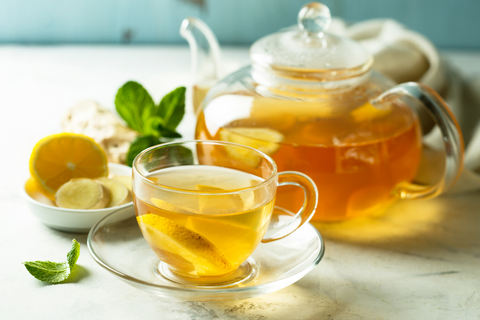 a glass teapot filled with lemon ginger honey tea sits beside a glass mug with tea in it.