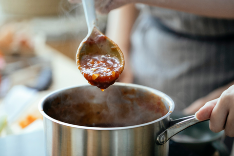 a big pot of tomato sauce with a wooden spoon dipped into it pulling out a scoop of sauce