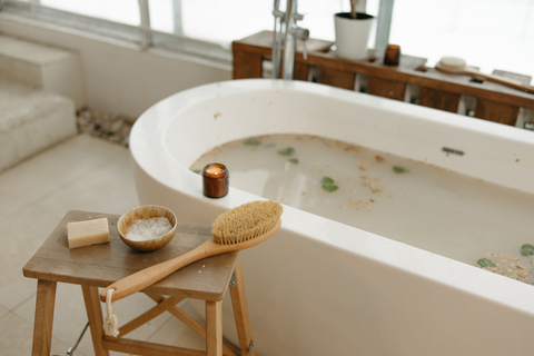 a wooden stool with a cowl of epsom salts sits beside a bathtub with epsom salts in it