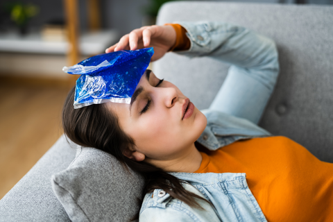 a person with an ice pack on their forehead lies on the couch