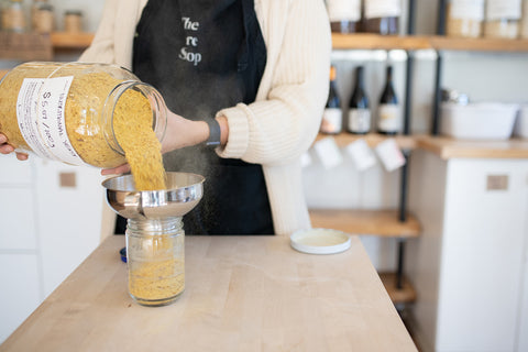 a person wearing a black apron fills a jar with nutritional yeast