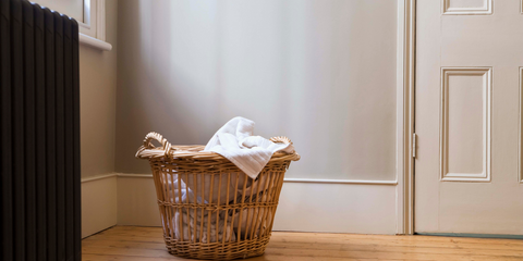 a laundry basket sits on a wooden floor. There's a black radiator to the left of the basket and a shut white door to the right of the basket.