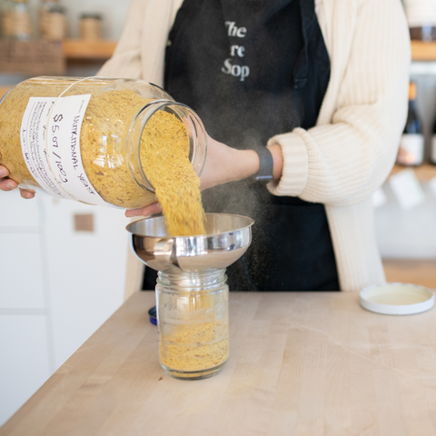 a person wearing a Tare Shop apron pours nutritional yeast from a big jar into a smaller jar
