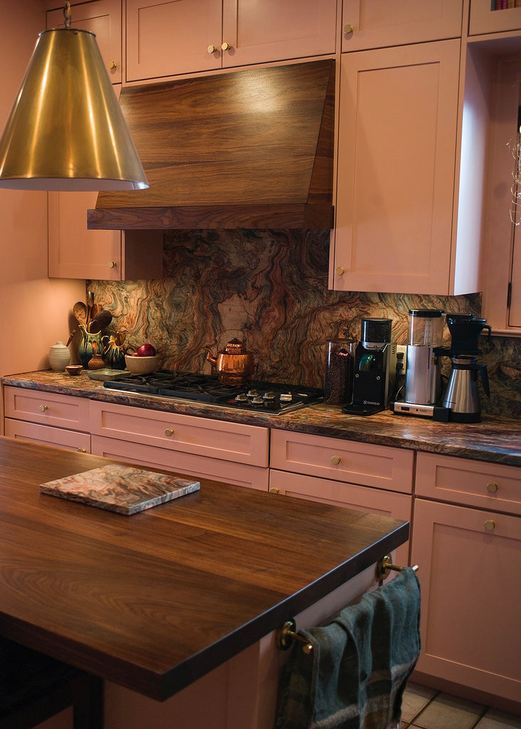 Warm, old world-inspired kitchen with pink cupboards and rich, blue and pink-swirled quartzite countertops and backsplash slab
