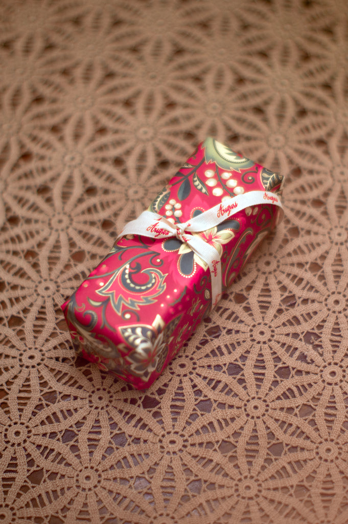 Deep pink paisley wrapped paper wrapped around a rectangular box and tied with a ribbon that says "Auguri"