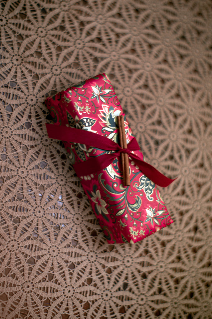 Gift wrapped in red patterned paper and tied with a red ribbon with an cinnamon stick tucked in by the bow