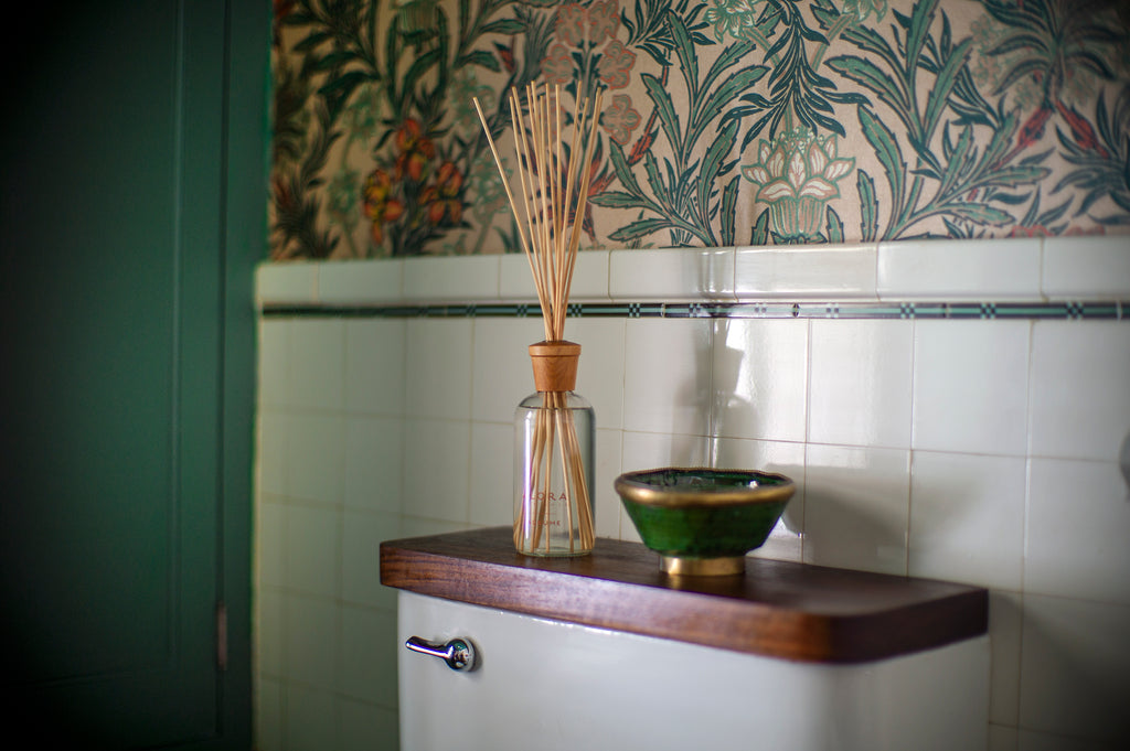 Reed diffuser on back of toilet seat in green bathroom