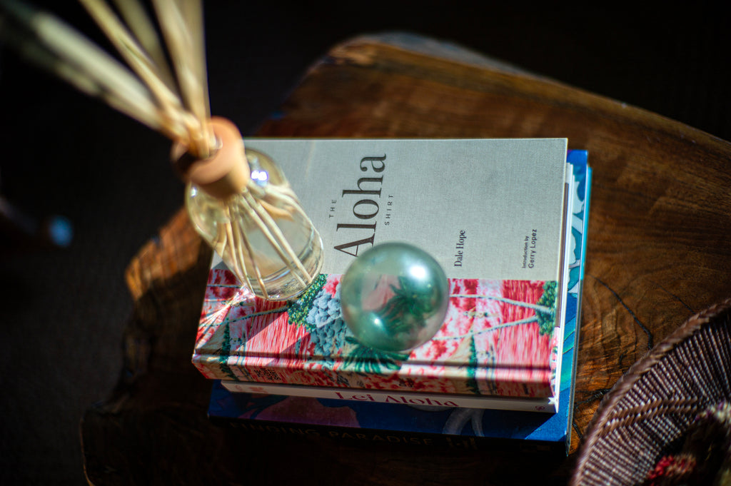 Isola reed diffuser sitting on a stack of Hawaiian themed books