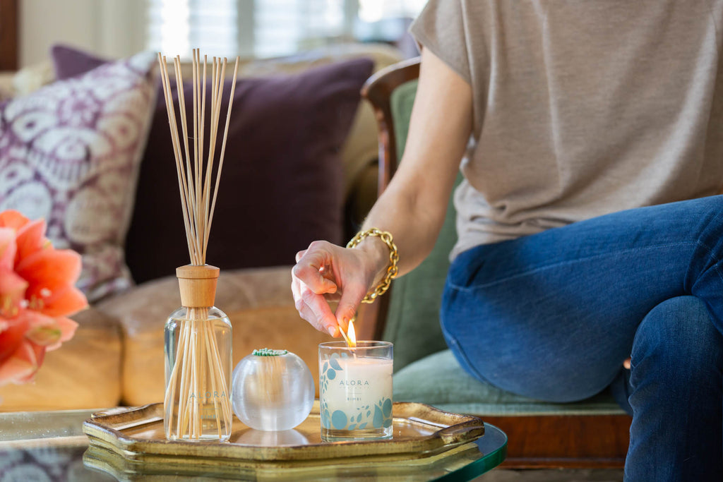 Woman lighting Bimbi candle on coffee table that's sitting next to a Bimbi reed diffuser