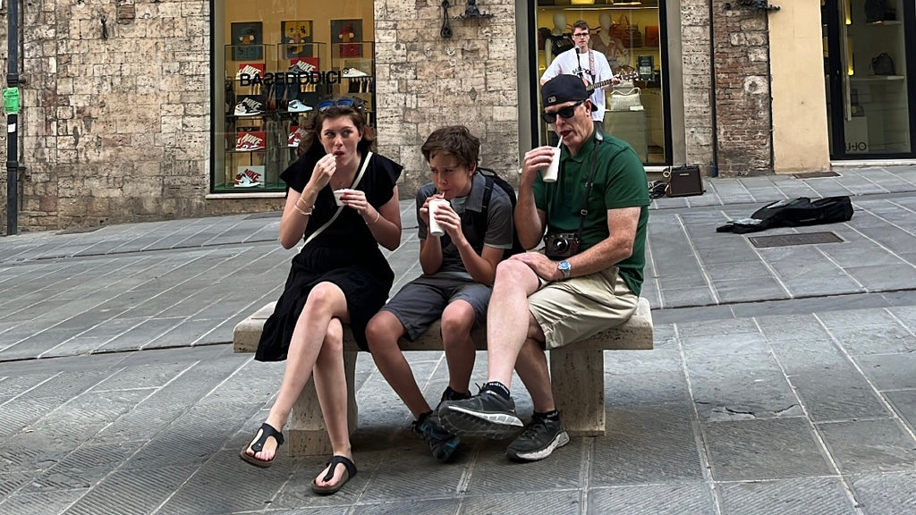 Girl, boy, and dad eating gelato on a bench on a street in Italy