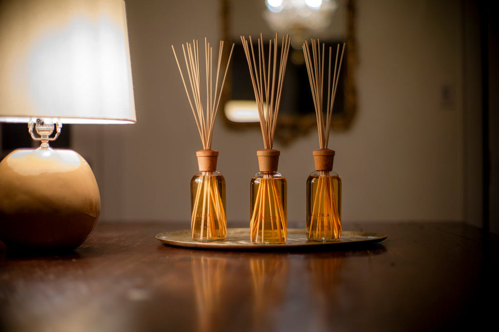 Three reed diffusers on a tray next to a lamp